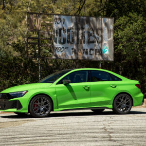 A green Audi RS3 next to a dilapidated sign