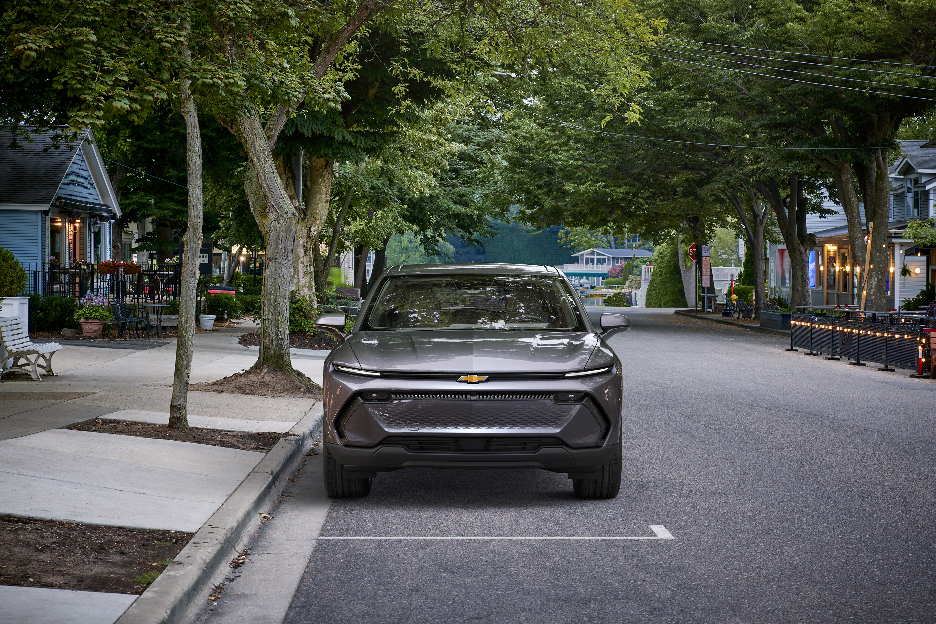 Front view of 2024 Chevrolet Equinox EV 1LT in Galaxy Gray Metallic parked on a street with trees. Preproduction model shown. Actual production model may vary. Visit chevy.com/EquinoxEV for availability.