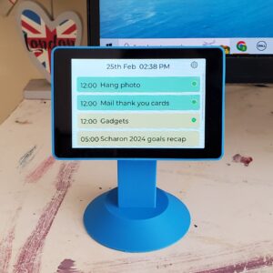 A blue DeskBuddy powered on and sitting on top of a desk, next to a computer monitor.