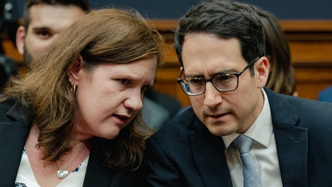 Federal Trade Commission Commissioners Rebecca Kelly Slaughter and Alvaro Bedoya sit at a table and chat with each other at a Congressional hearing.