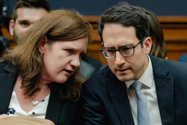 Federal Trade Commission Commissioners Rebecca Kelly Slaughter and Alvaro Bedoya sit at a table and chat with each other at a Congressional hearing.