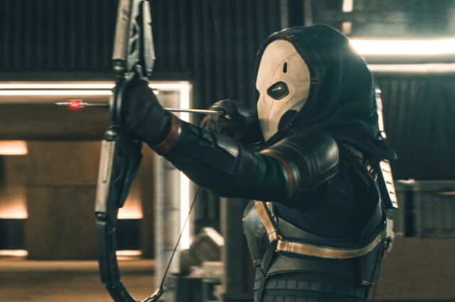 masked figure all in black firing a high-tech bow and arrow