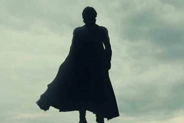 Black shadowy figure in superhero garb floating in mid air