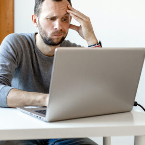 young man looking puzzled working at laptop