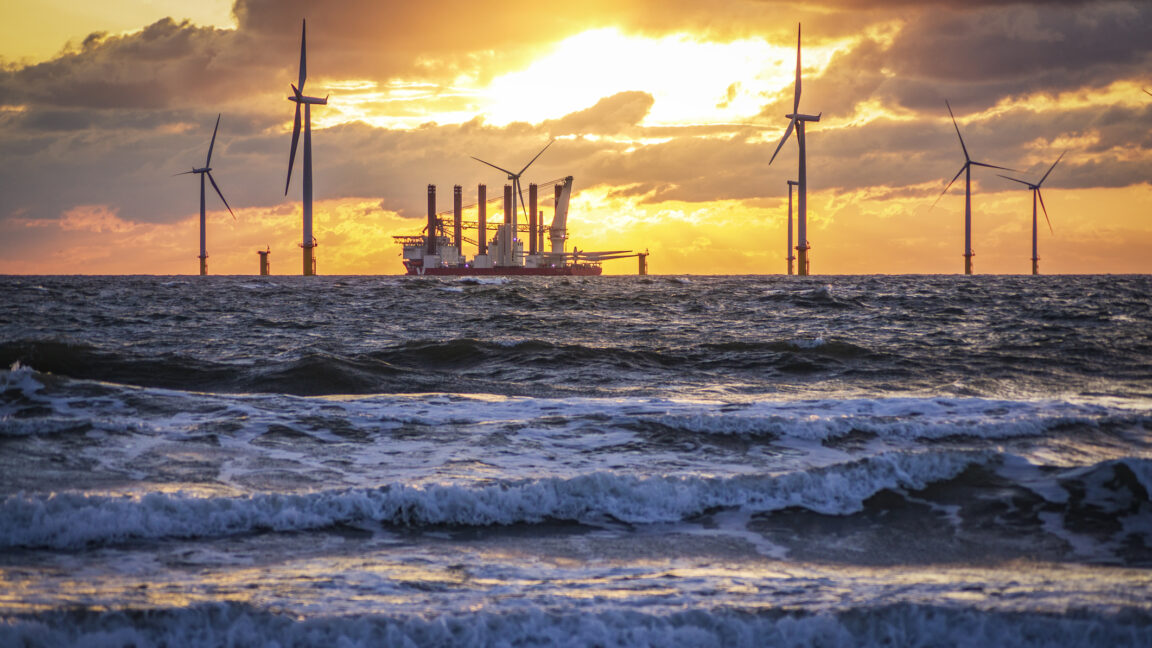 gentle waves are in the foreground, was a ship sits among wind turbines, carrying the parts for additional ones.