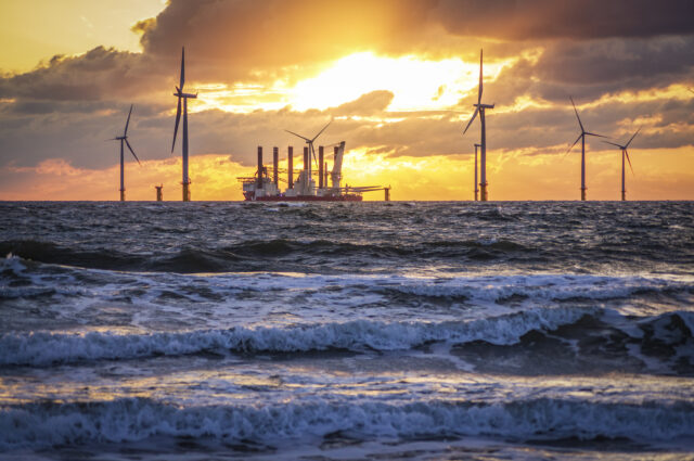 gentle waves are in the foreground, was a ship sits among wind turbines, carrying the parts for additional ones.