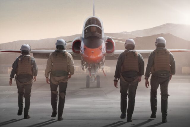 backs of four fighter pilots walking toward a fighter jet