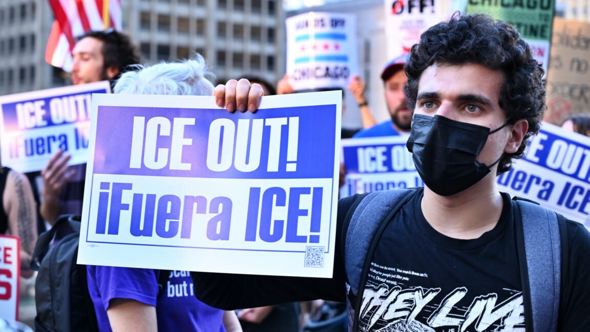 A protestor holds a sign that says "ICE OUT!"