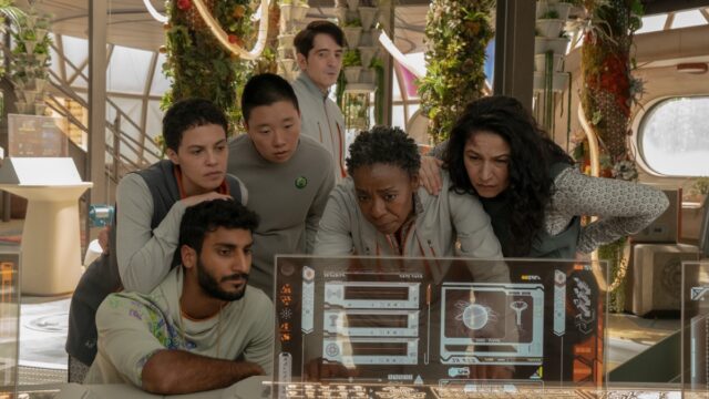 group of ethnically diverse people in space habitat uniforms gathering around a computer monitor
