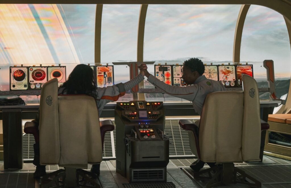 two crew members viewed from behind, sitting at control panel of a ship, high-fiving