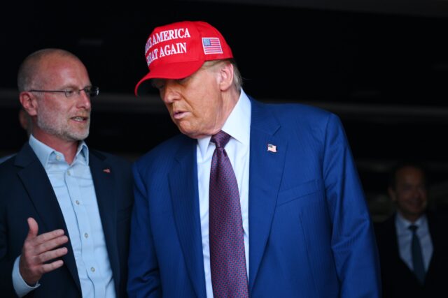 FCC Commissioner Brendan Carr standing next to and speaking to Donald Trump, who is wearing a "Make America Great Again" hat.